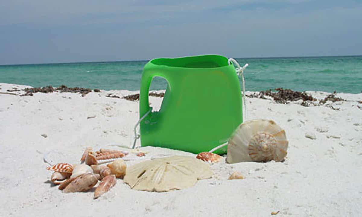 A sand bucket made out of a plastic laundry container sitting on the beach.