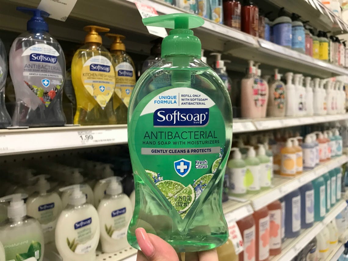 A pump bottle of Softsoap antibacterial hand soap being held in front of a shelf of more hand soap at Target.
