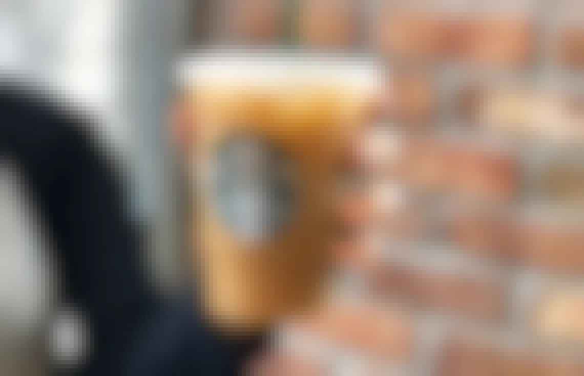 A person holding up a Starbucks iced coffee in front of a brick wall.