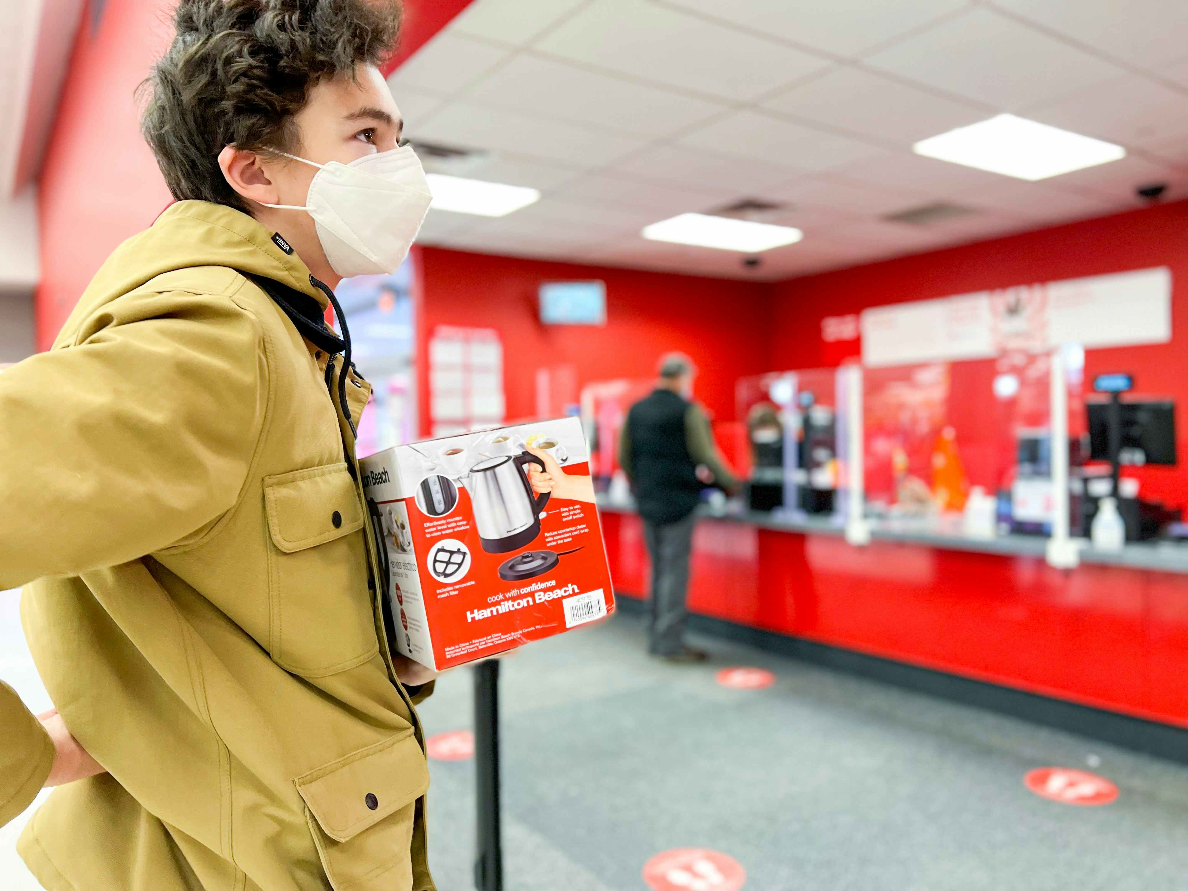 a person holding a hamilton beach kettle box in line at target customer service