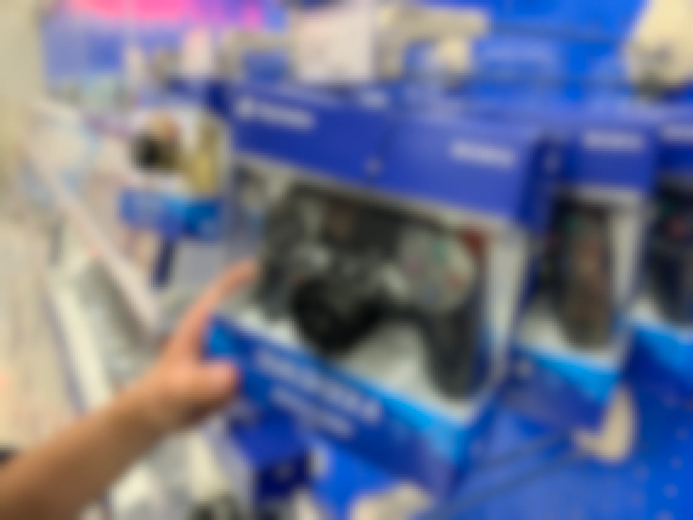A person's hand taking a packaged PS4 controller from the shelf at Target.