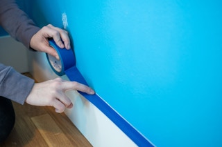 someone putting painters tape on baseboard