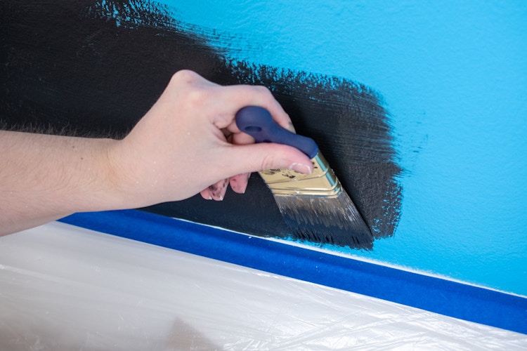 someone painting wall next to tape on baseboard