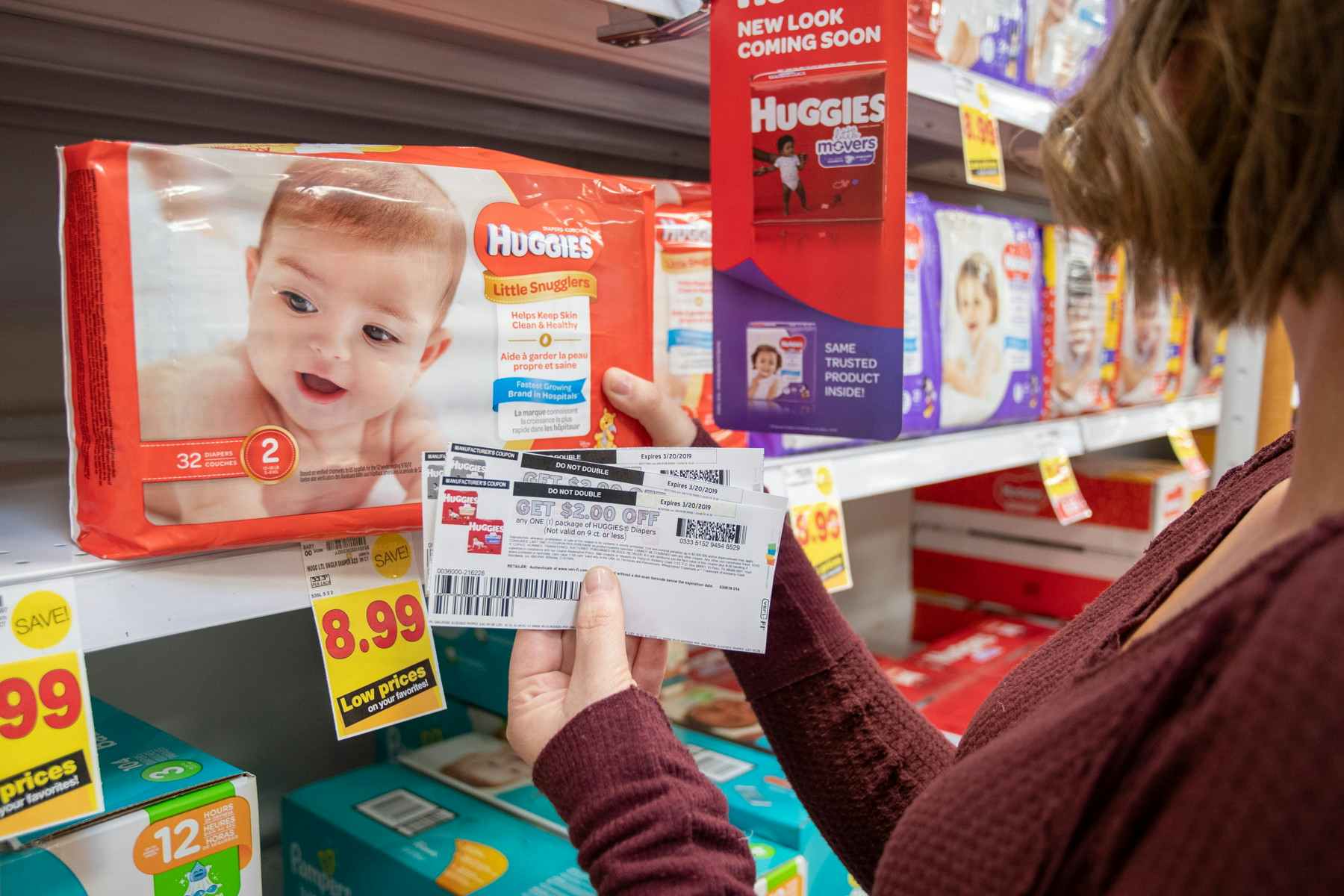 A woman holding Huggies coupons near diapers on display in a store