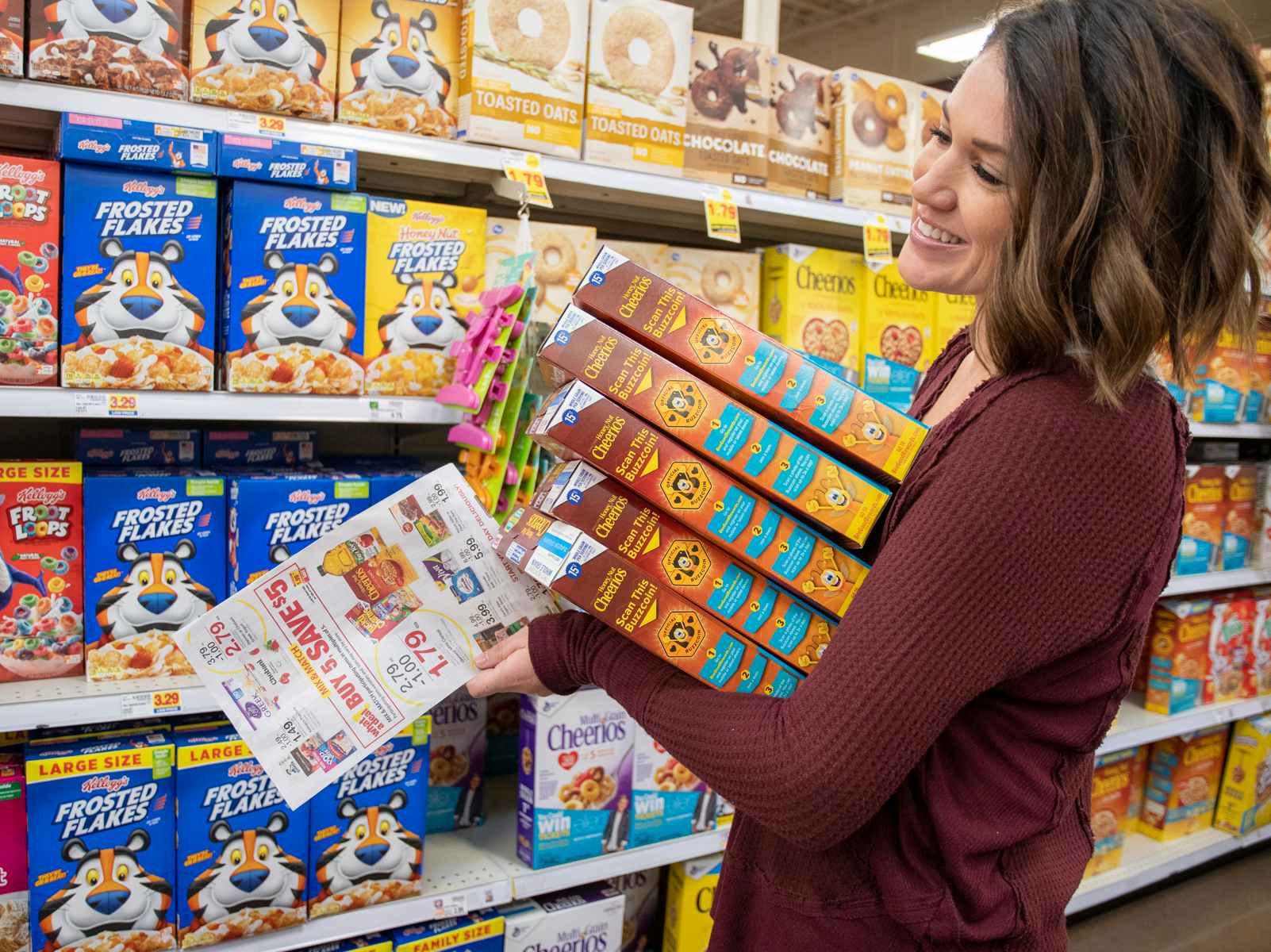 Woman holds stack of cereal boxes in cereal aisle smiling widely