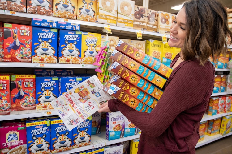 Woman holds stack of cereal boxes in cereal aisle smiling widely