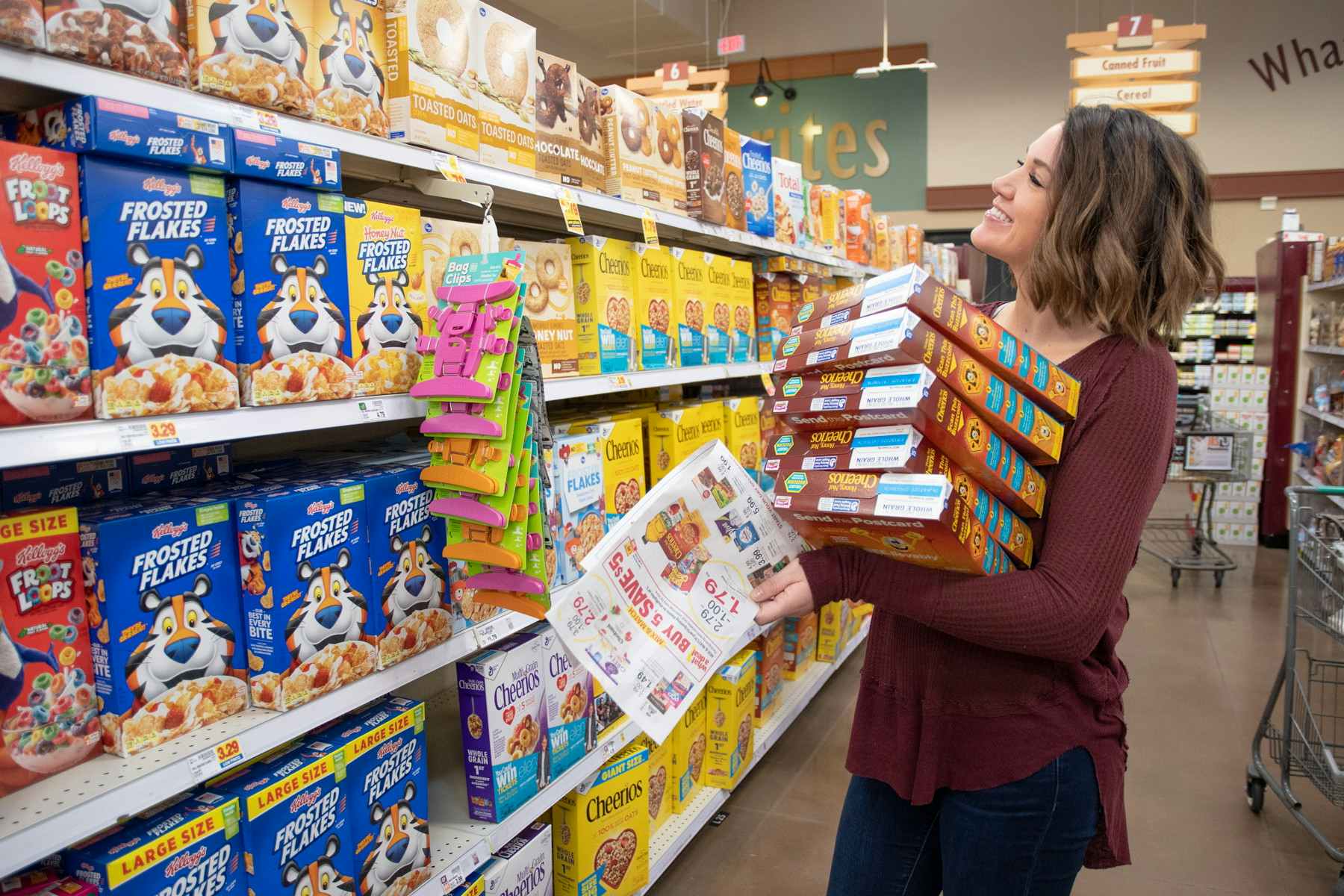 A woman holding multiple boxes of cereal in her arms while standing in the cereal aisle.