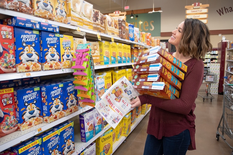 woman holds multiple boxes of cereal in her arms while standing in the cereal aisle