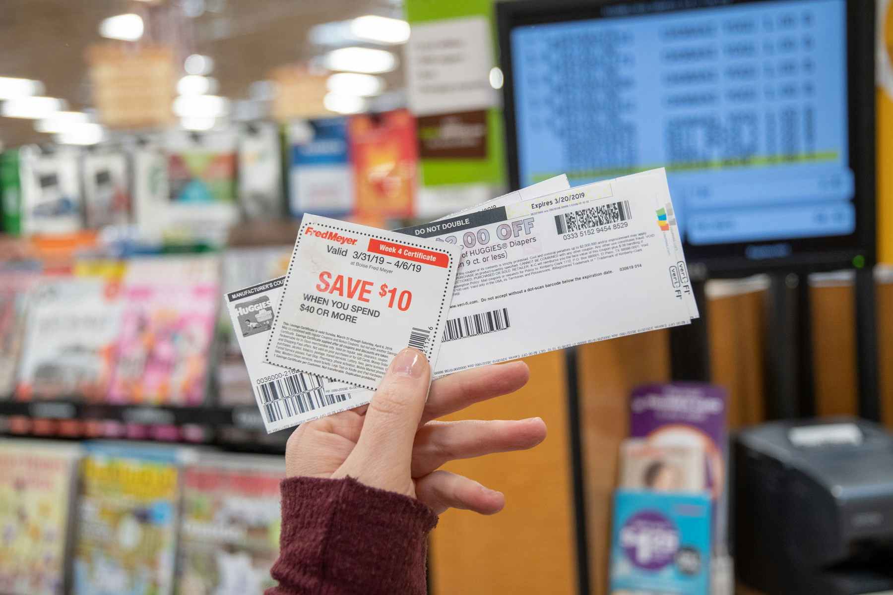 A person holding up printed coupons in front of a checkout register.