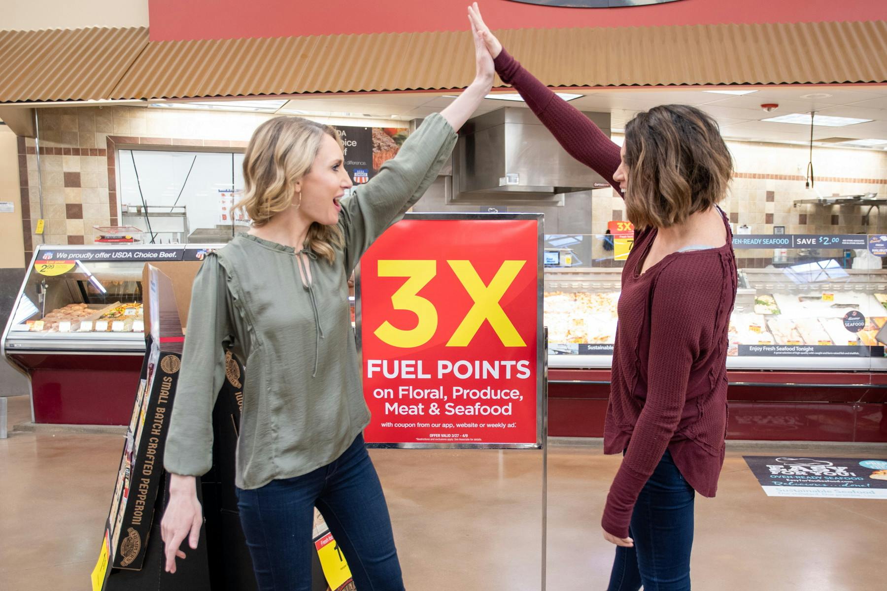 two women high five over a Kroger fuel rewards 3x points sign