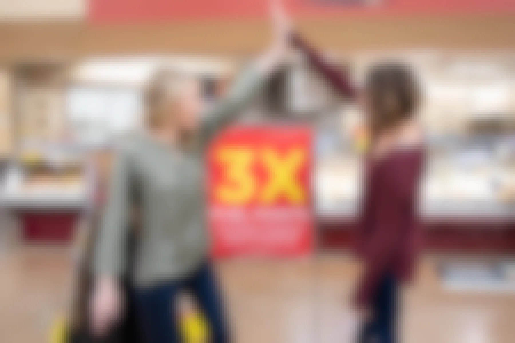 two women high five over a Kroger fuel rewards 3x points sign