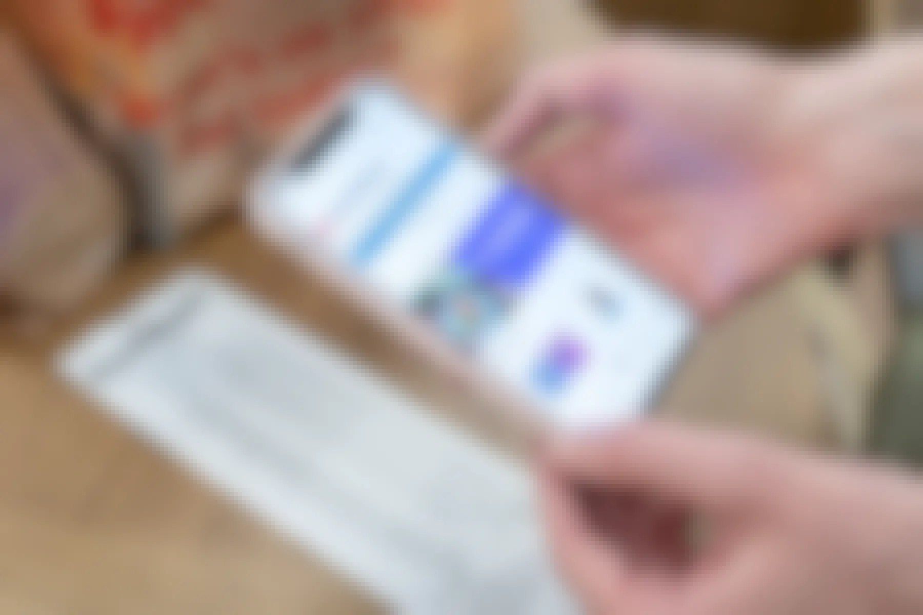 A person's hands holding an iPhone with the Ibotta mobile app open about to scan a receipt that is on a table next to two bags of groceries.