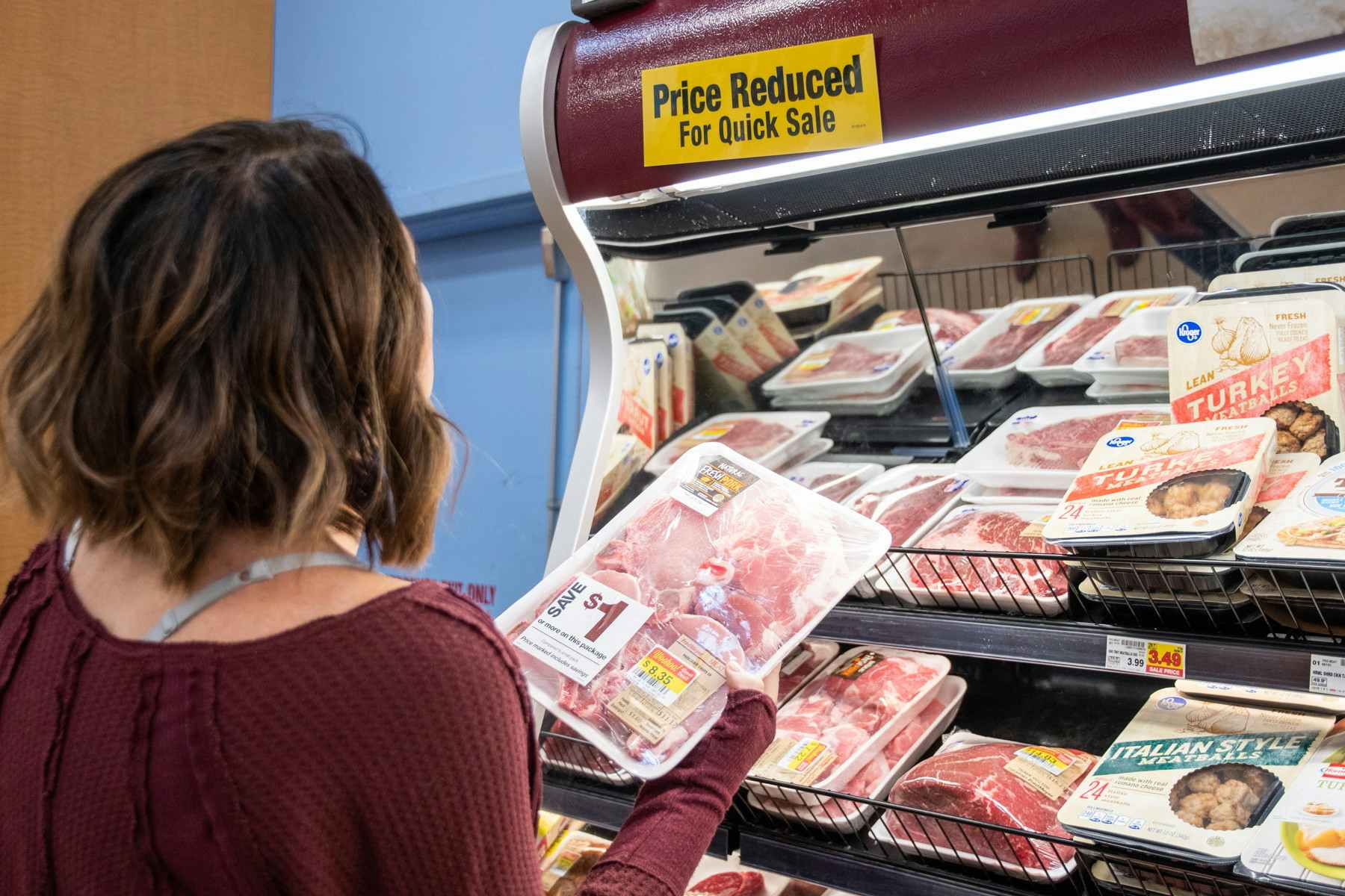 A woman looking at meat in the price reduced section.