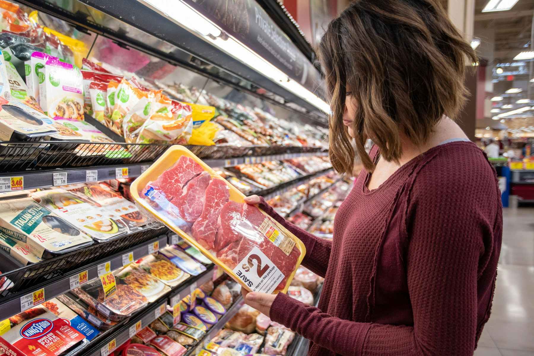 woman looking at meat in a grocery store meat aisle