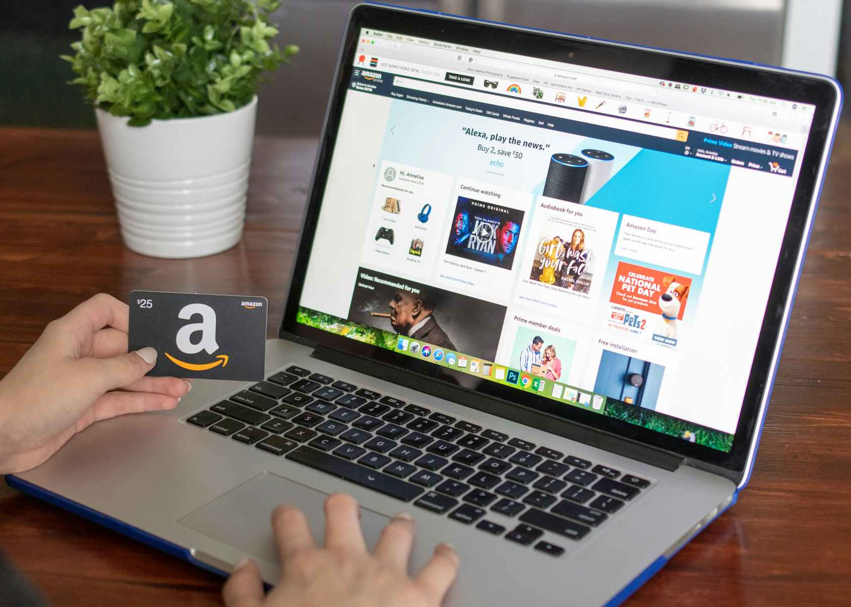 A person using a laptop displaying the Amazon website and holding an Amazon gift card.