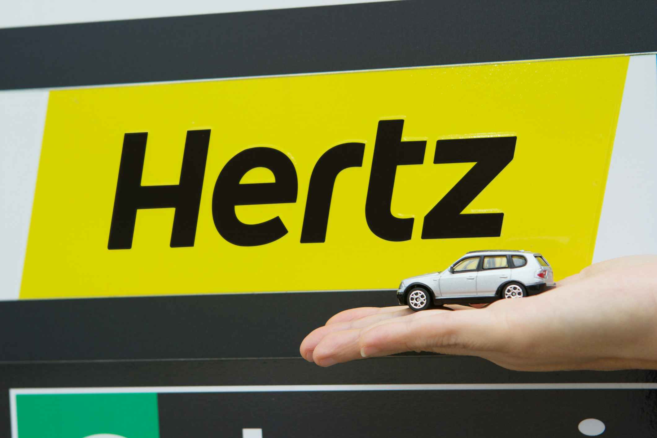 hand in front of hertz sign holds a small model car
