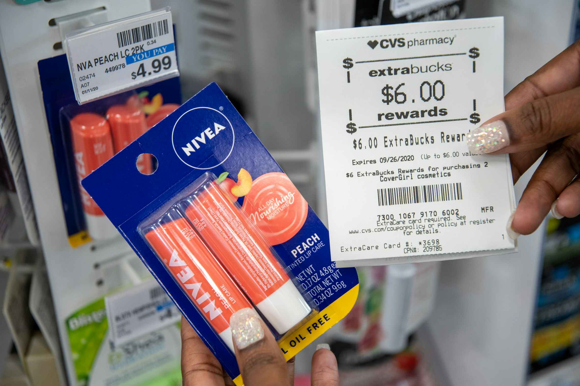 A woman holding CVS Extrabucks rewards for $6 next to Nivea lip balm next to a price tag that says, $4.99.