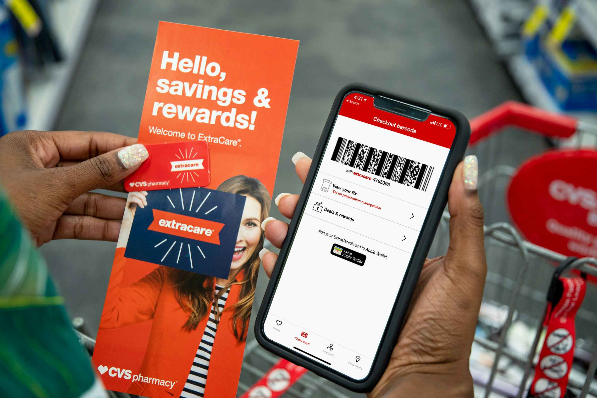 A person's hands holding an iPhone with the CVS app, a CVS rewards key chain card, and an CVS extracare rewards pamphlet while standing in an aisle at CVS.