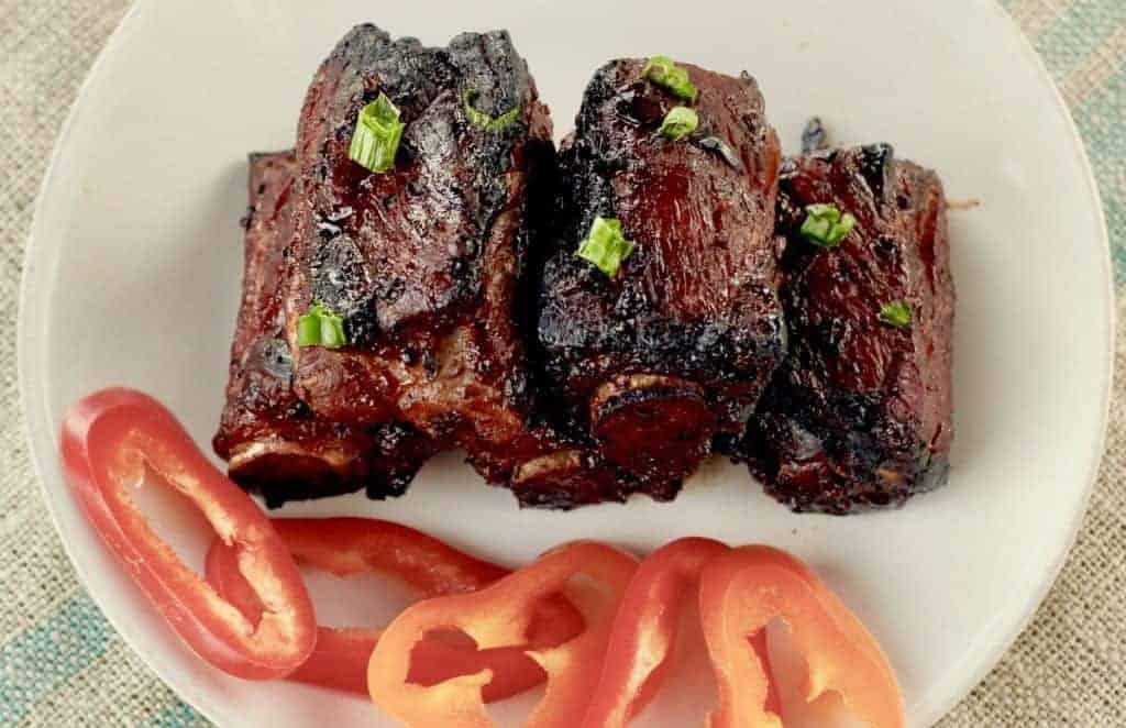 Slightly charred spare ribs on a plate with red peppers