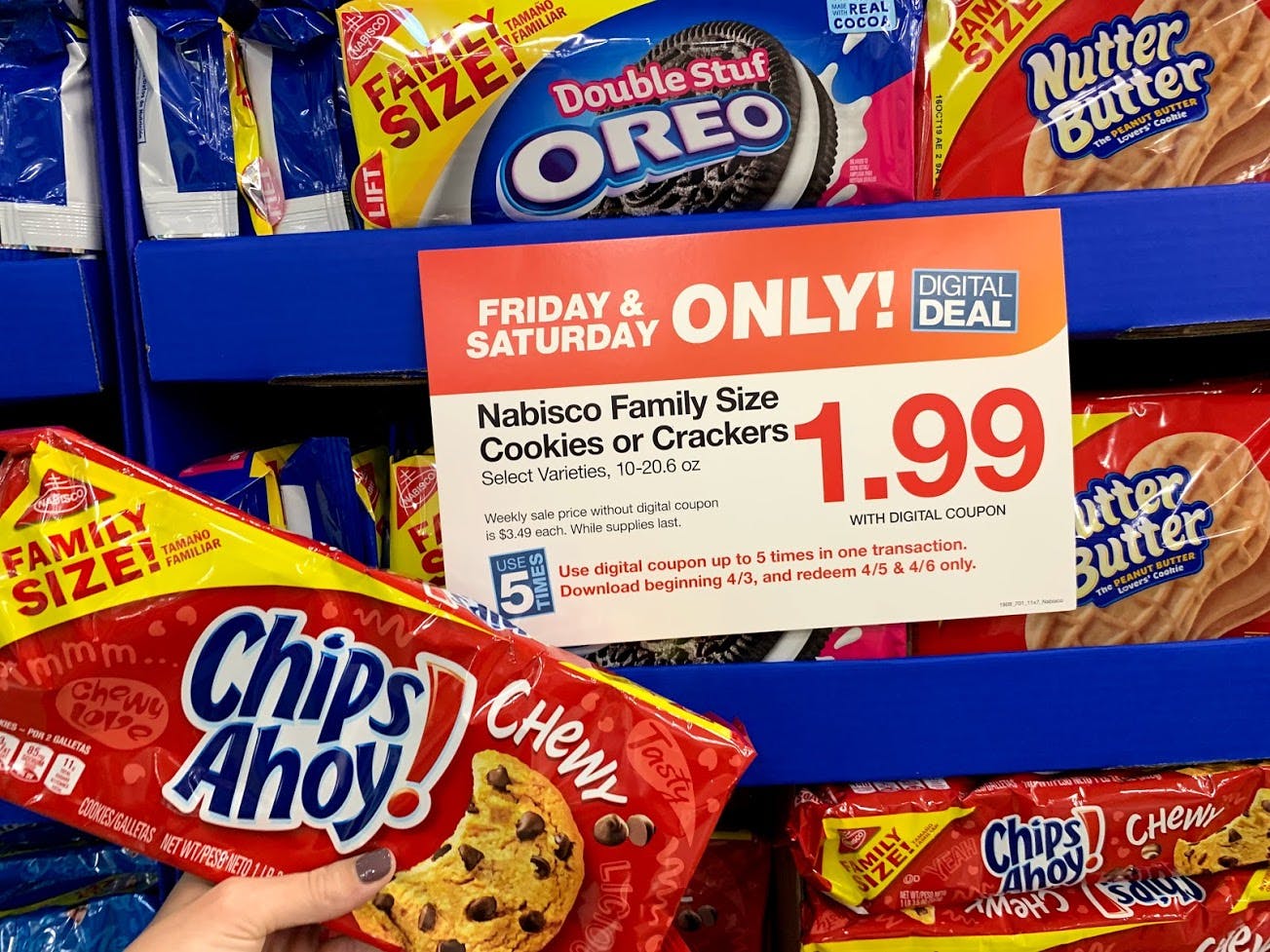 A person holding a package of Chips Ahoy cookies in front of a a sale sign on a store shelf that has packages of Oreos on it.