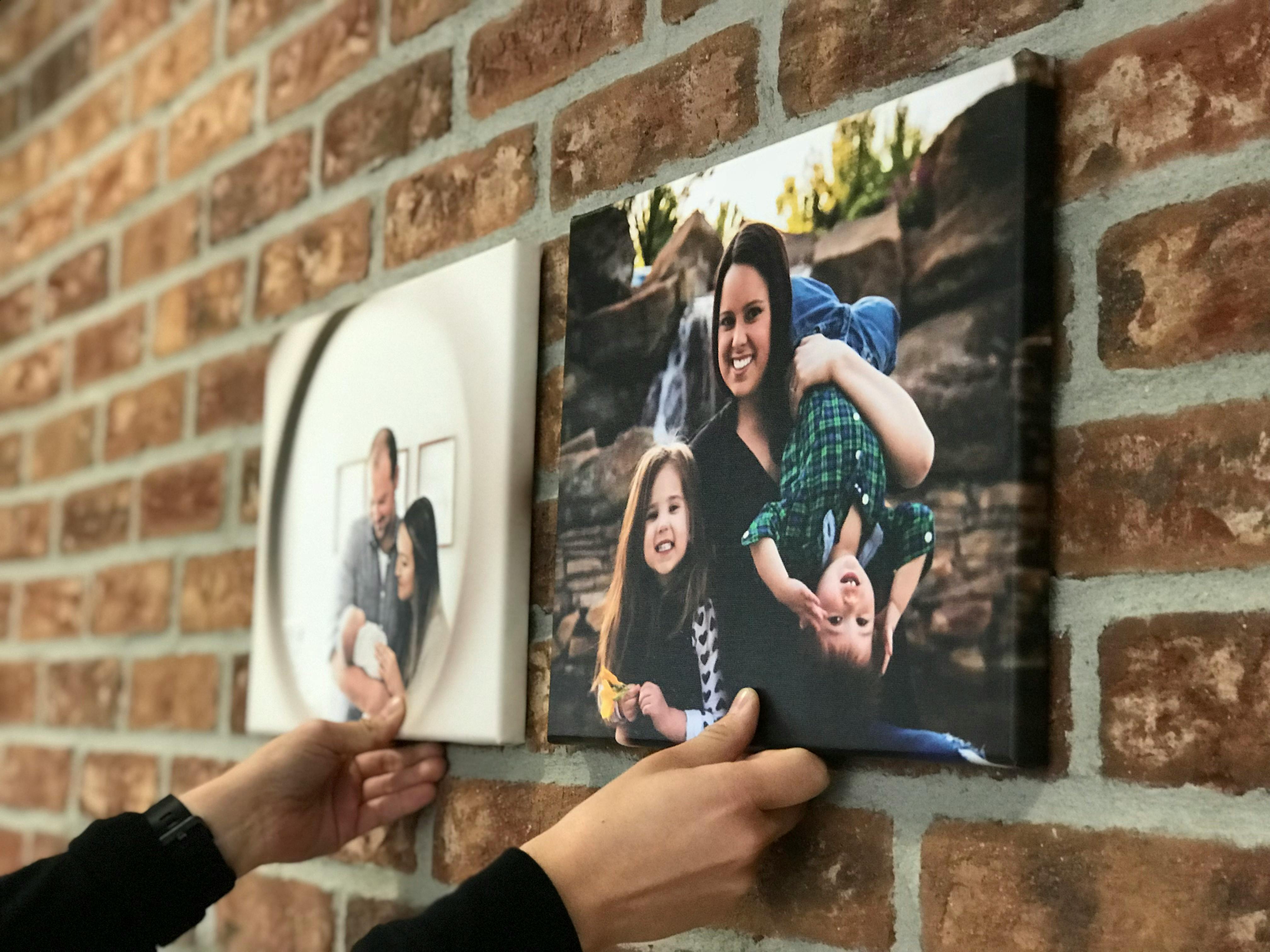 A person holding two pictures up to a wall.
