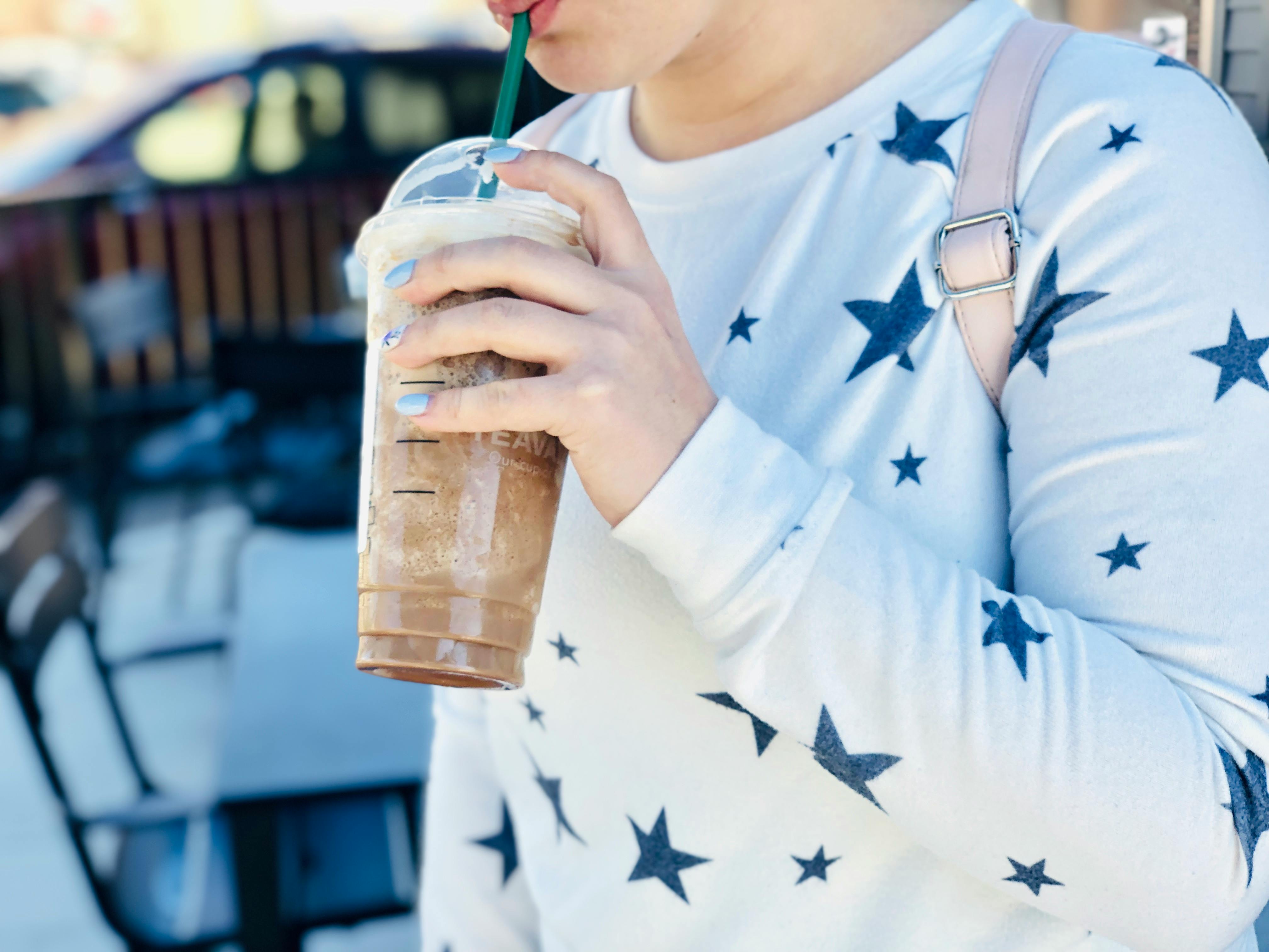 A woman holding a frozen blended Starbucks drink, drinking from the straw.