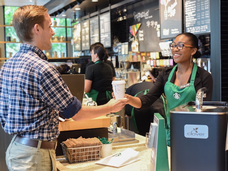 A barista handing a customer a Starbucks drink.