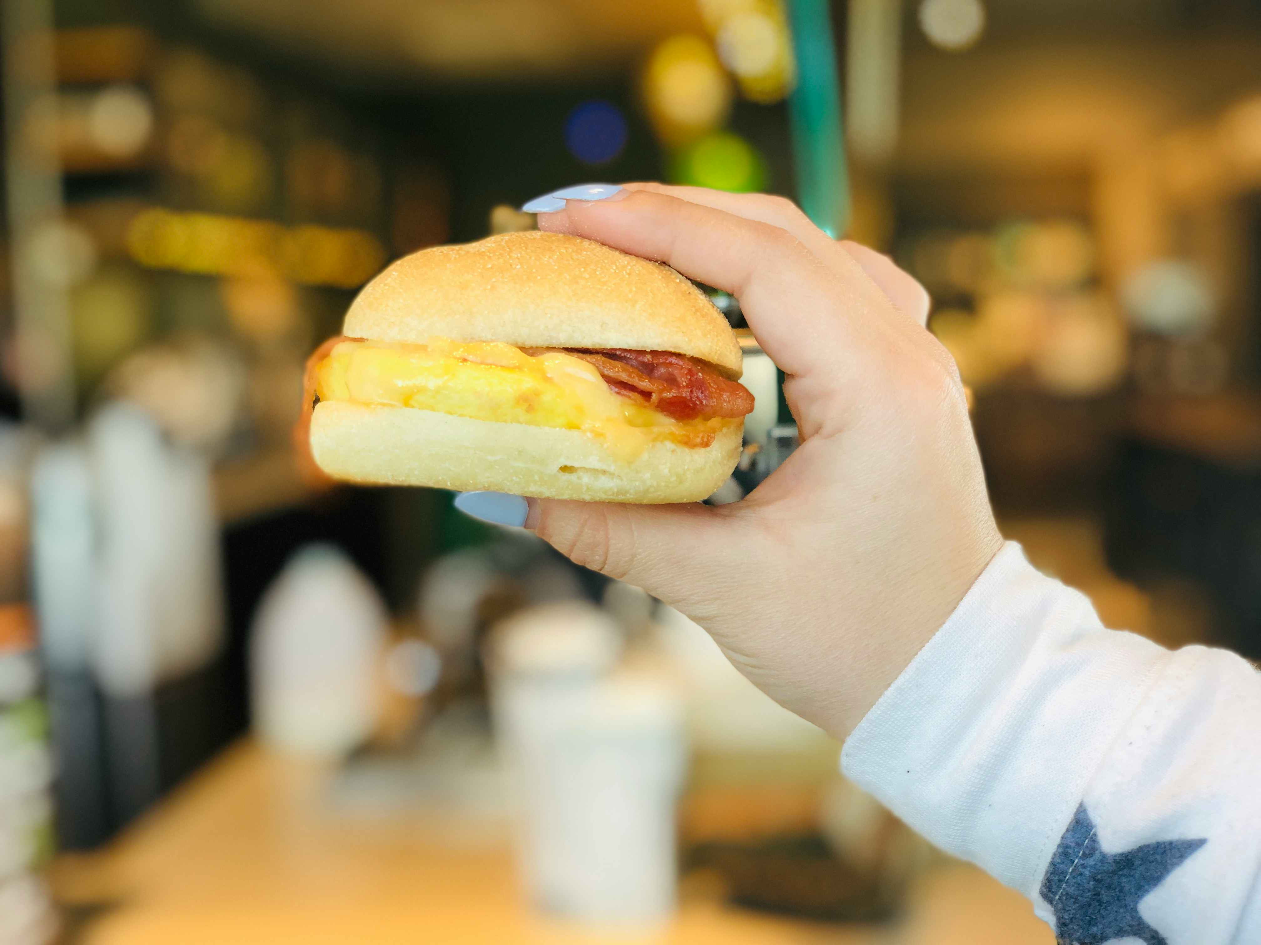A person's hand holding up a Starbucks breakfast egg bacon sandwich.