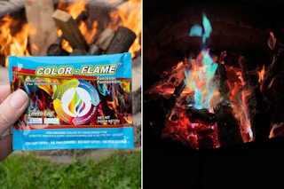 A person's hand holding up a Color-Flame packet in front of an open fire pit, and a fire glowing blueish in the dark. 