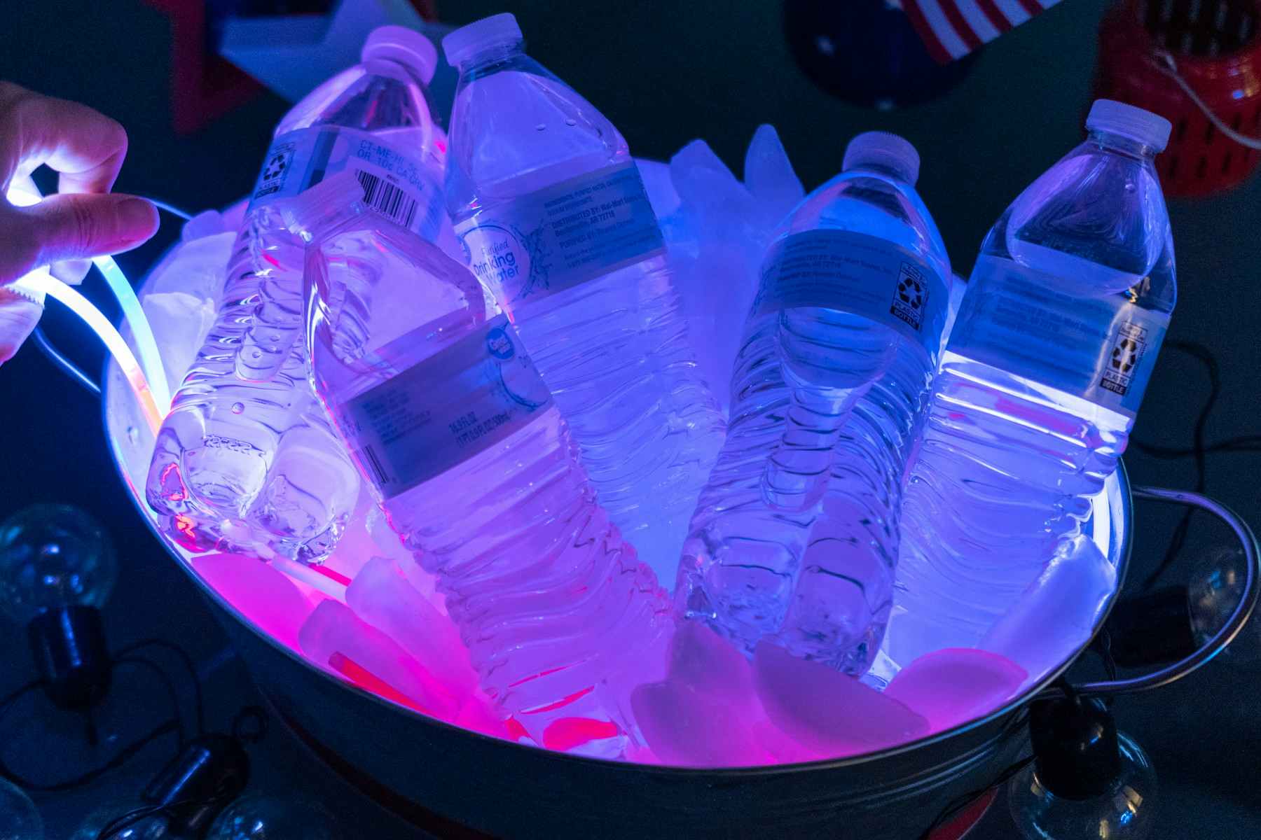 A drink cooler filled with ice and water bottles glowing with red, white, and blue glow sticks.