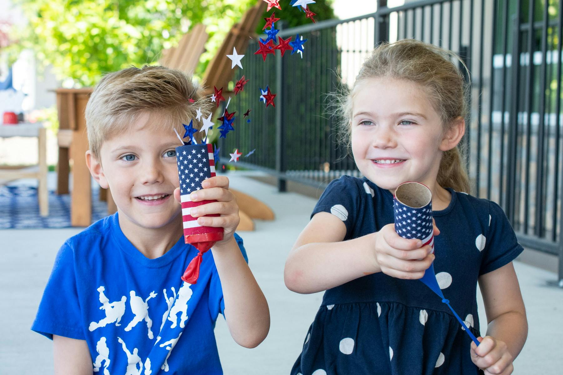 Two children sitting and shooting out confetti from their confetti poppers made with toilet paper rolls, balloons and flags.
