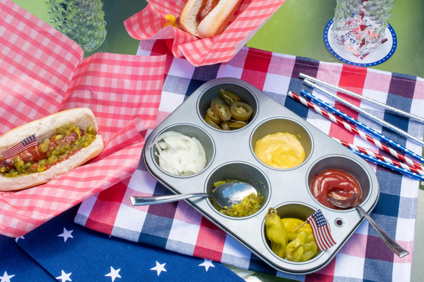 A muffin pan filled with different condiments sitting on a table decorated for the 4th of July.