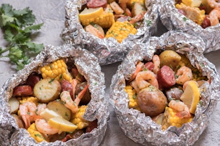 Aluminum foil with potatoes, shrimp, sausage, corn on the cob, lemon, and melted butter inside.