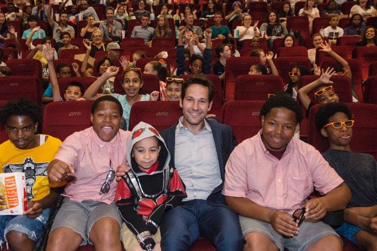 A group of kids sitting in a movie theater with Paul Rudd, looking excited.