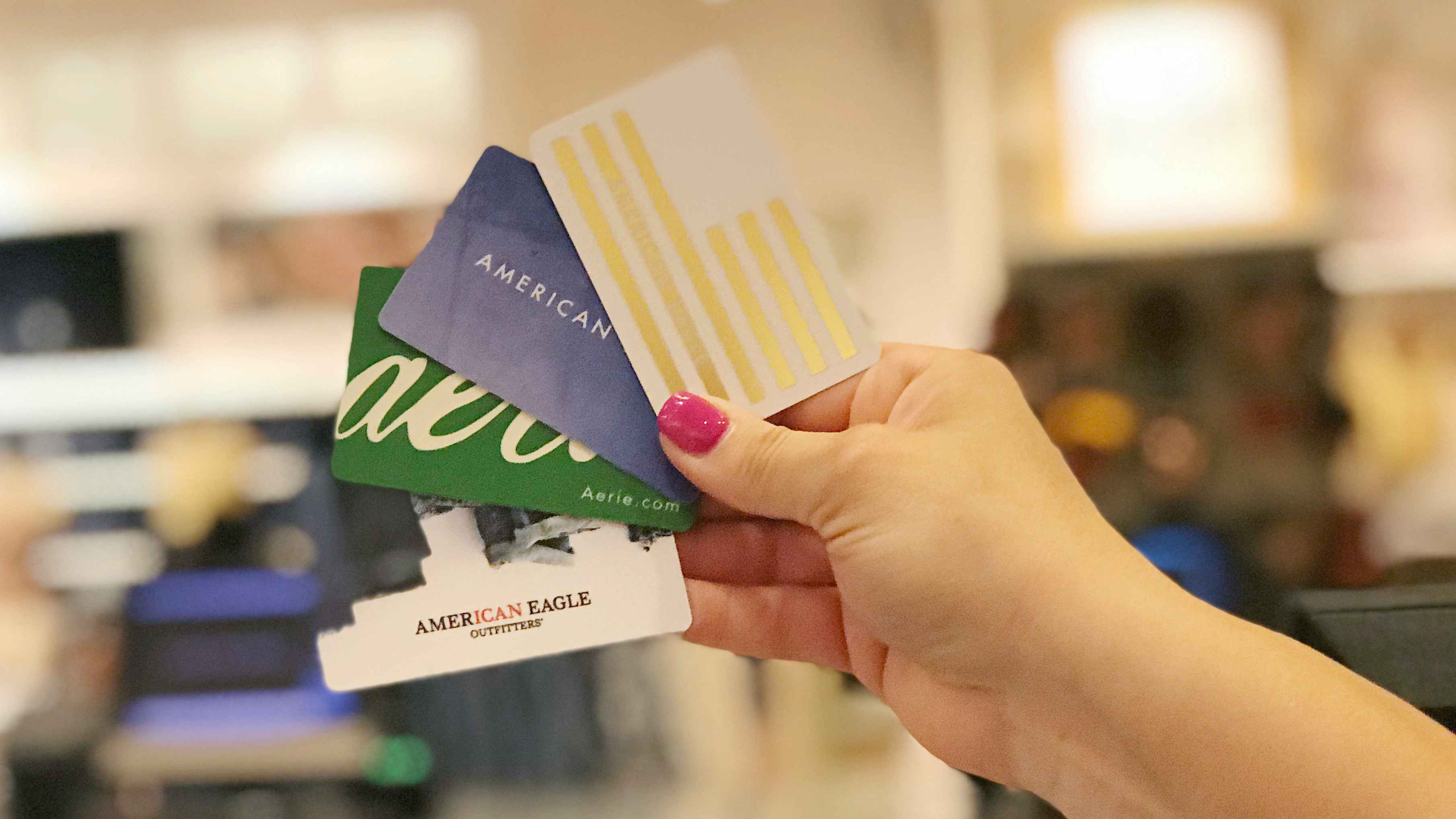 a woman holding up multiple american eagle and aerie gift cards in the store