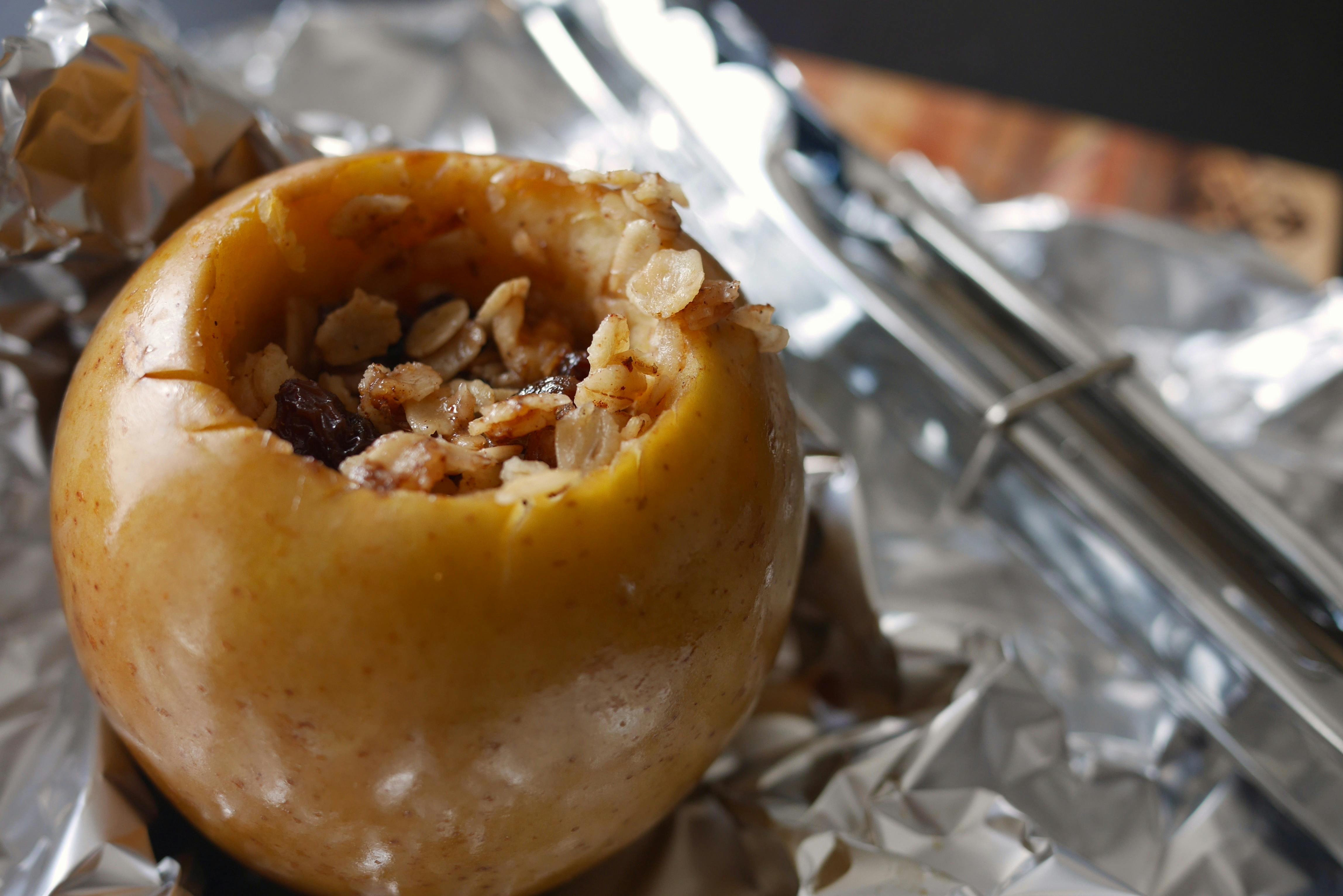 An apple sitting on foil that's filled with granola and raisins 