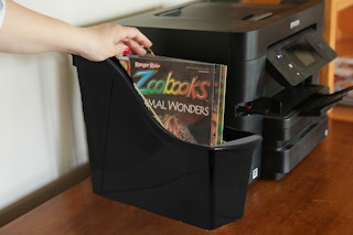 A person organizing books into a Dollar Tree magazine holder. 