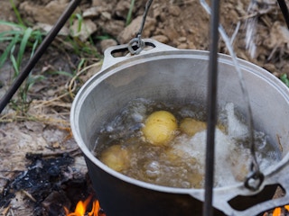 Potatoes boiling in water in a pot hung over I campfire