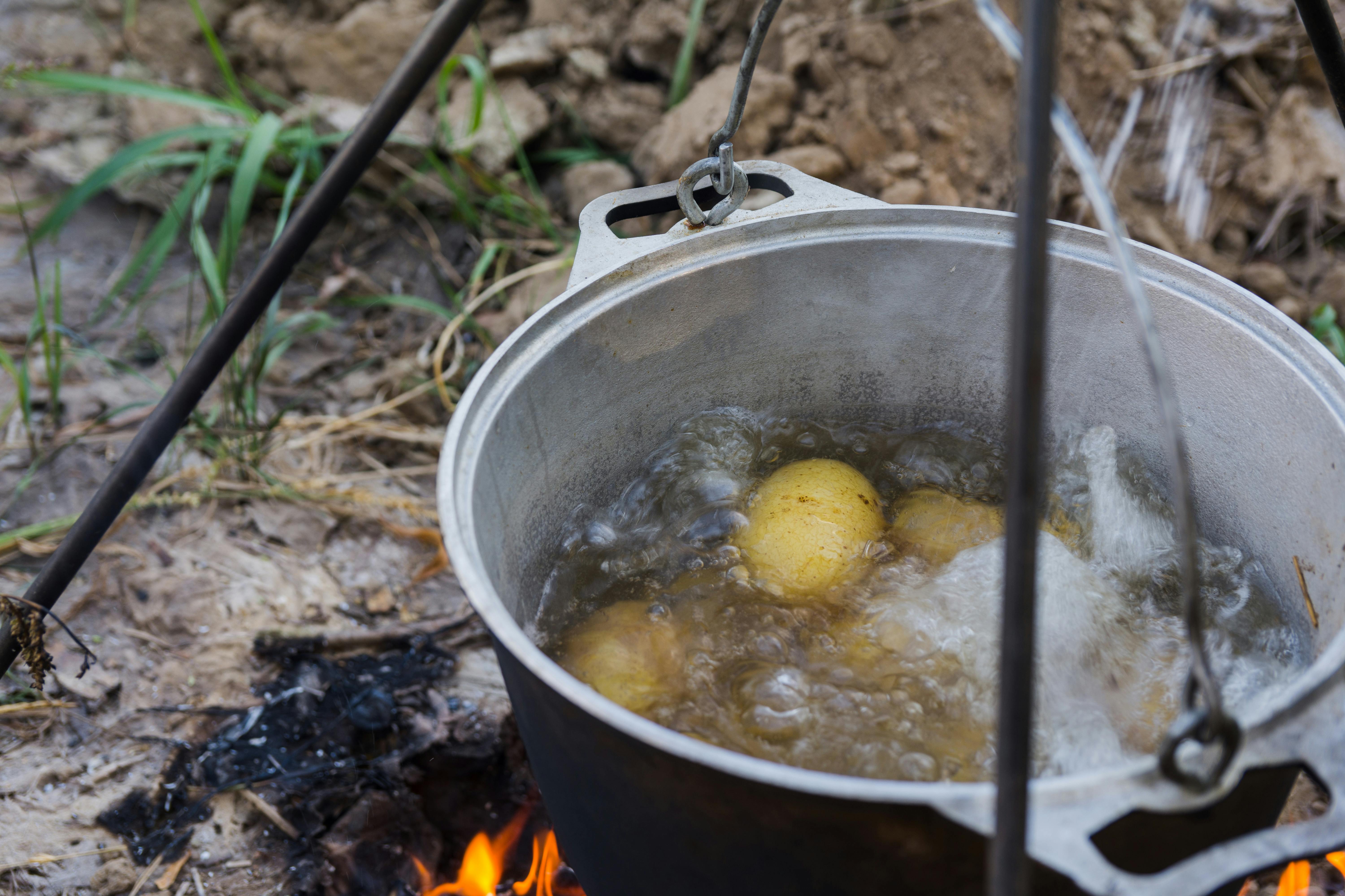 Potatoes boiling in water in a pot hung over I campfire