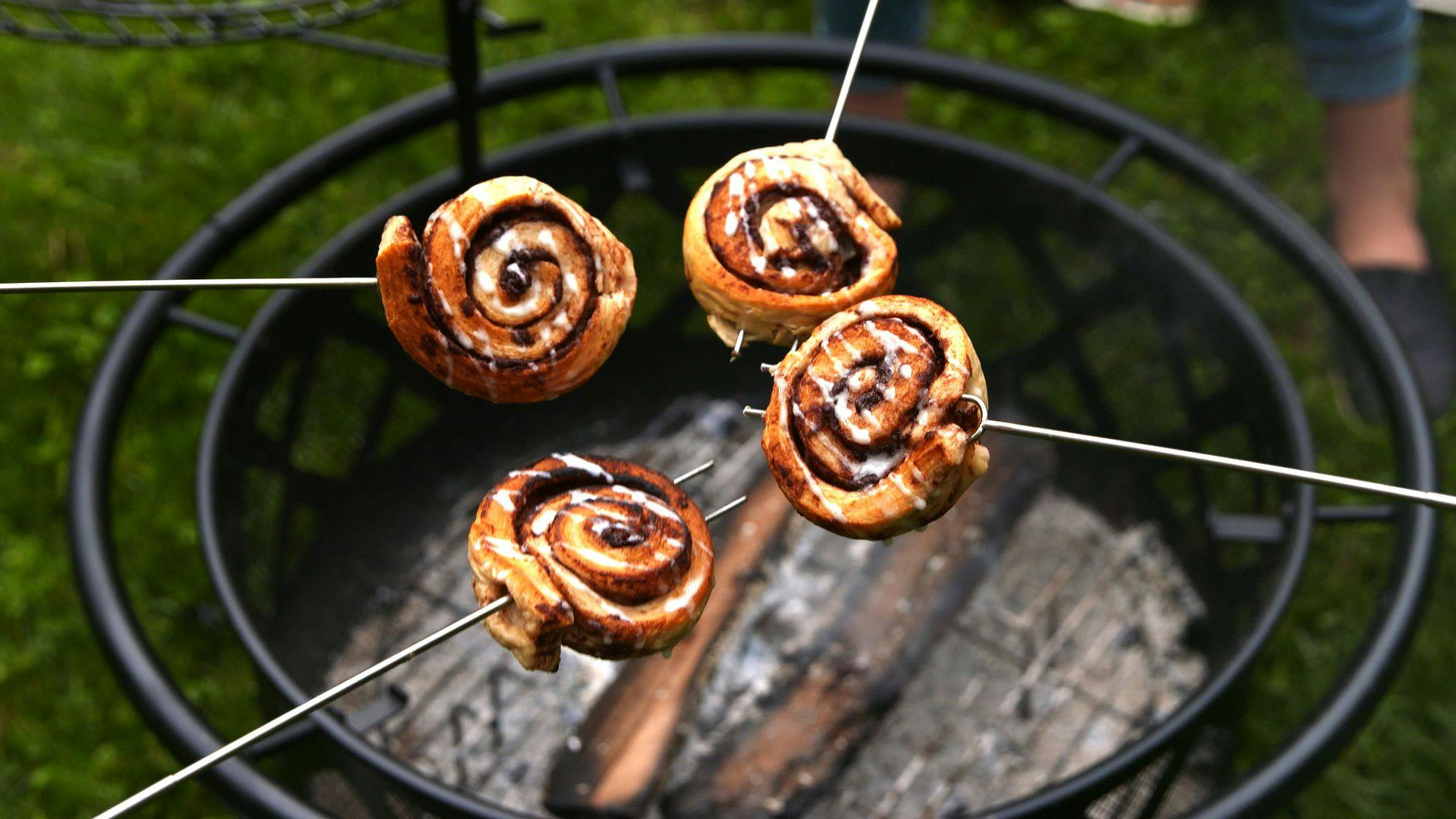 Cinnamon rolls on sticks being cooked over a grill