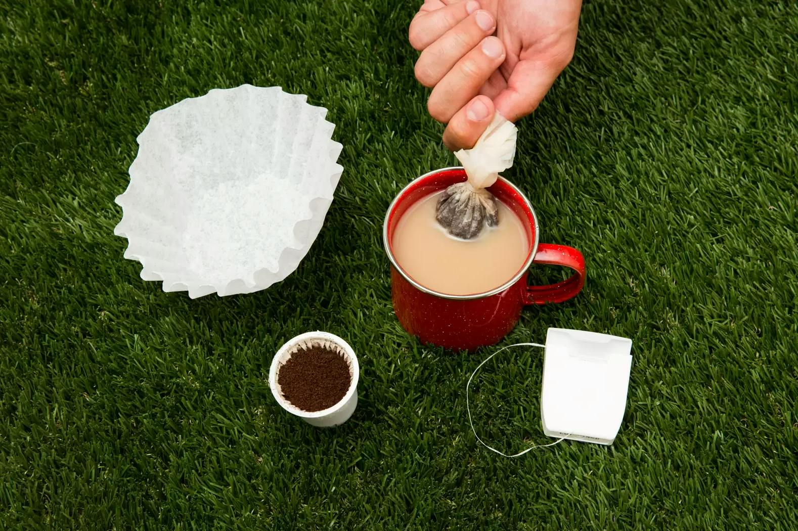 A person dipping coffee grounds wrapped in a coffee filter into a coffee mug.