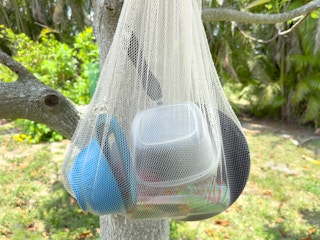 A mesh bag filled with dishes hanging in a tree to dry