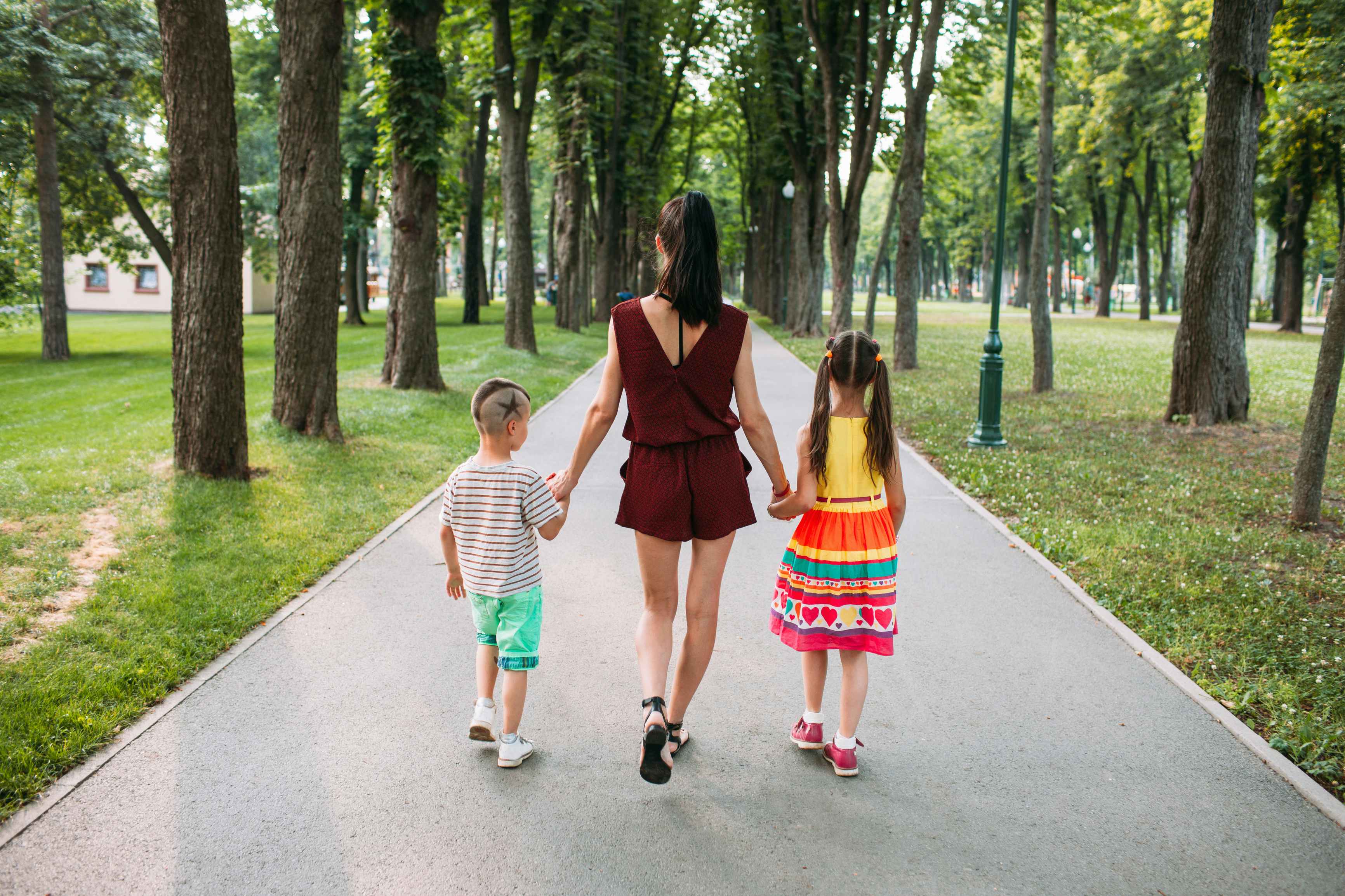 A parent walking through a park, holding the hands of two children