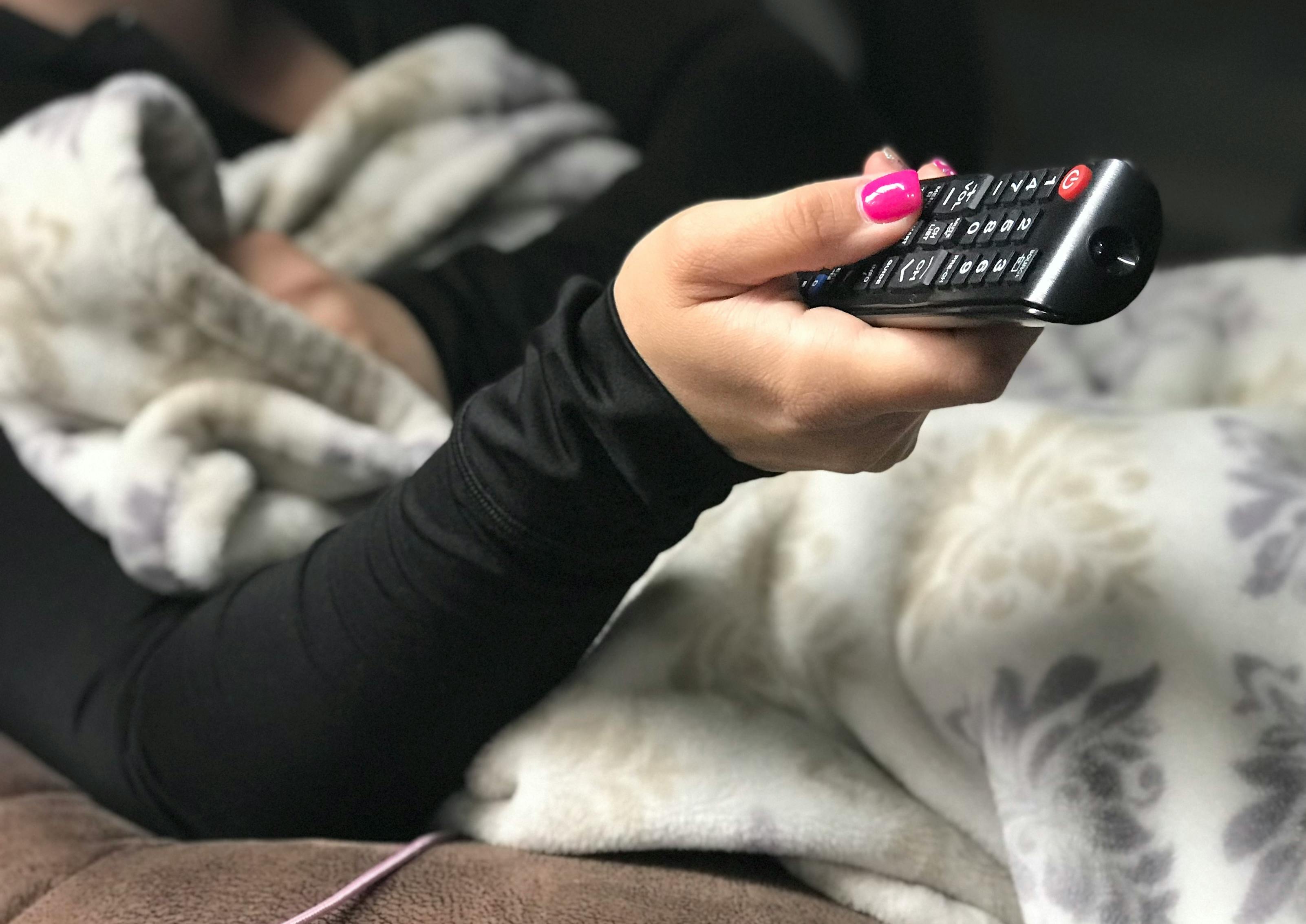 person sitting on couch with blanket holding remote
