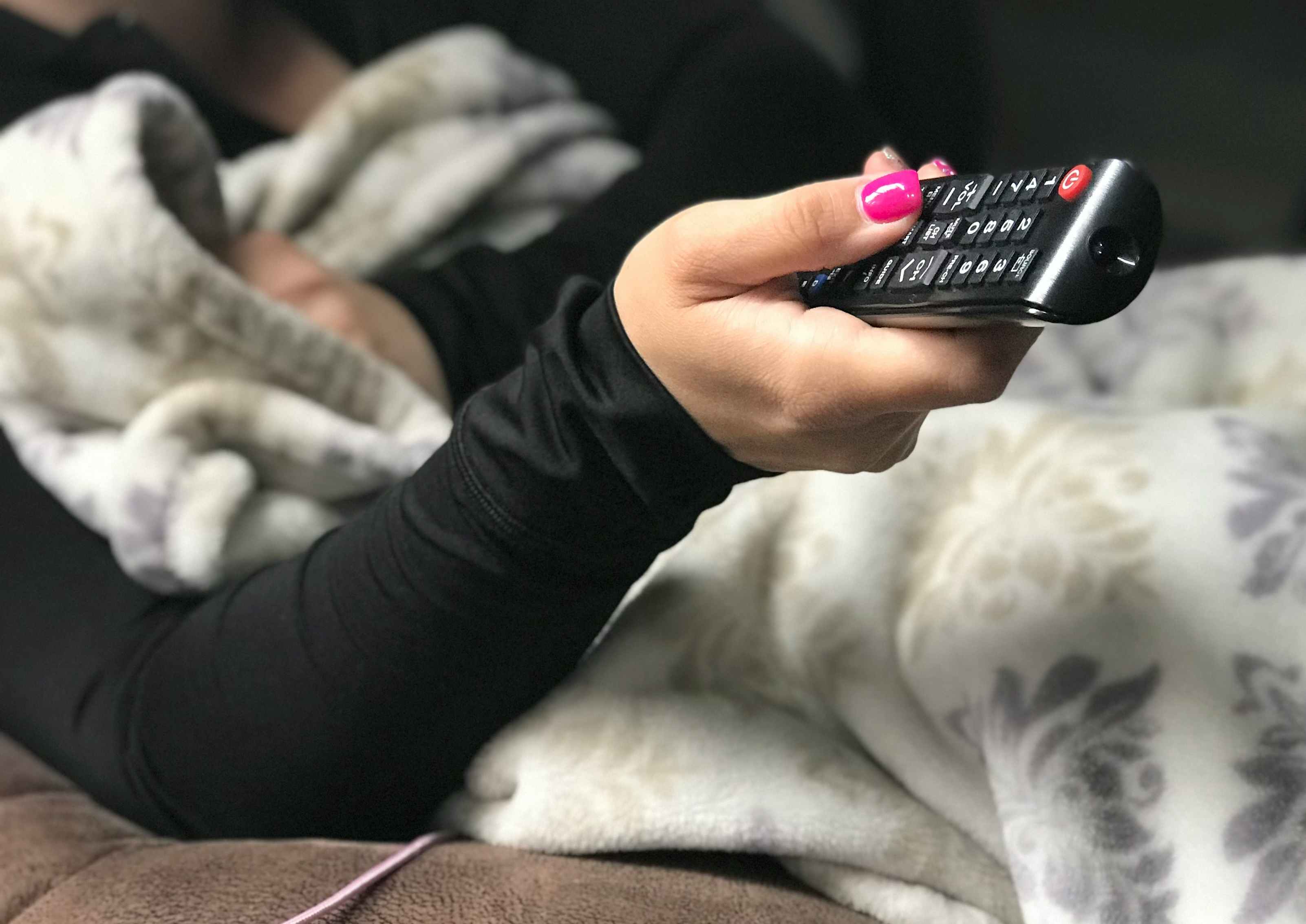 A person sitting on a couch with a blanket, holding a remote.