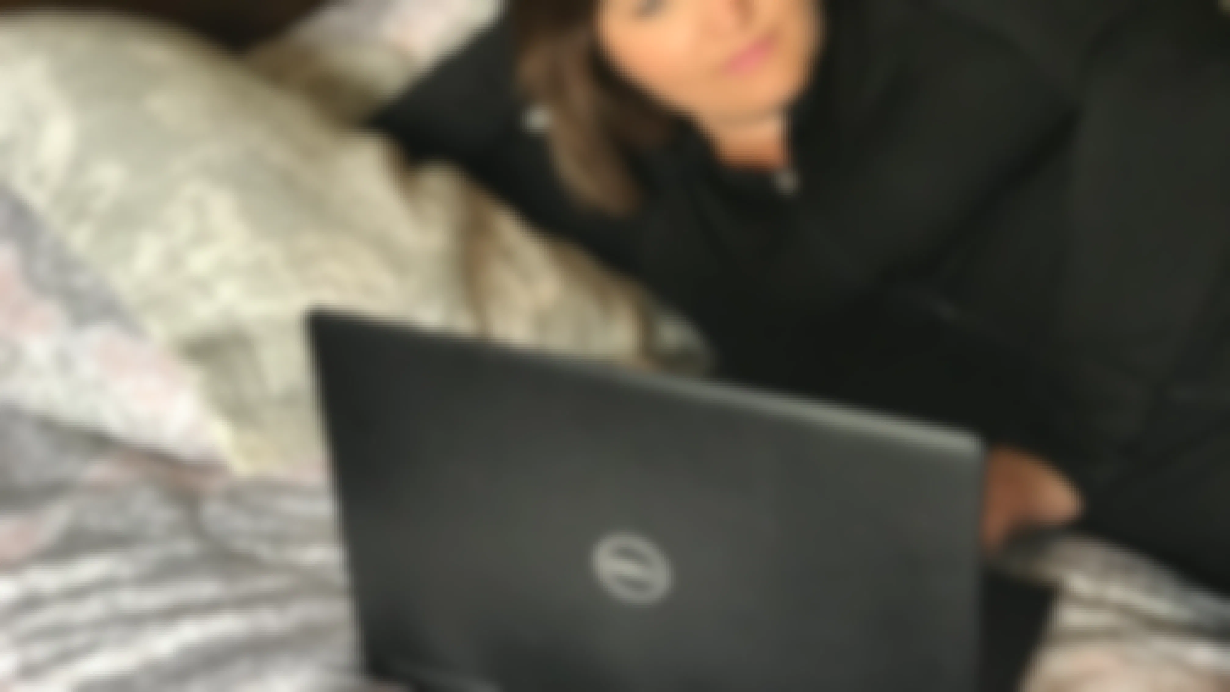 A woman laying on a bed looking at something on a laptop