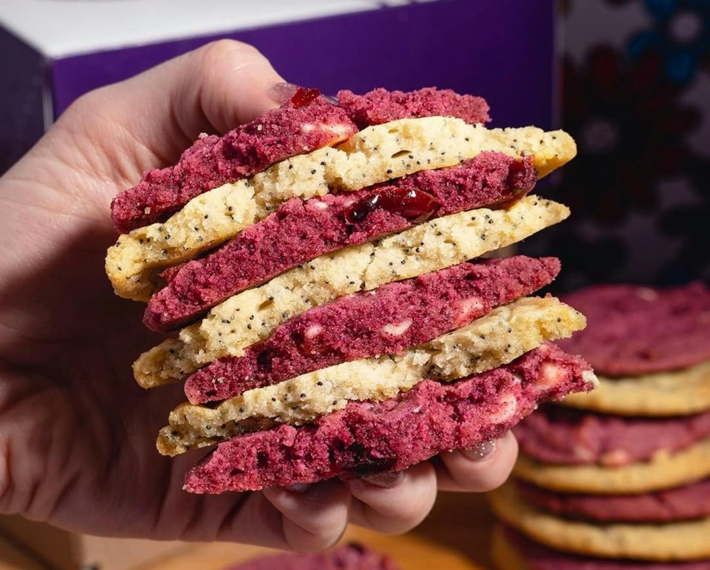 A person's hand holding a stack of Insomnia Cookies of alternating flavors.