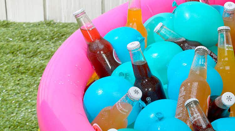 Glass bottled drinks sitting in an inflatable kid pool in the backyard with some chilled water balloons being used as ice packs.