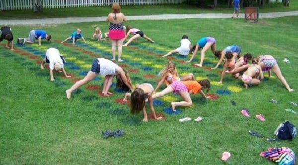 A group of children playing a giant game of DIY Twister on a lawn. The colored circles are painted on the lawn with spray paint.