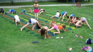A group of children playing a giant game of DIY Twister on a lawn. The colored circles are painted on the lawn with spray paint.